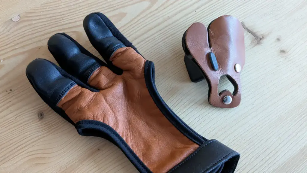 Schießhandschuh mit verstärkten Fingerkuppen und Fingertab nebeneinander auf einem Holztisch
