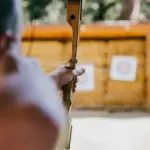 Ein Bogenschütze in Nahaufnahme. Im Hintergrund Zielscheiben.